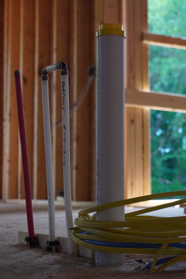 Capped drain stack and PEX stub-ups at a window opening, with coiled line stacked on the deck