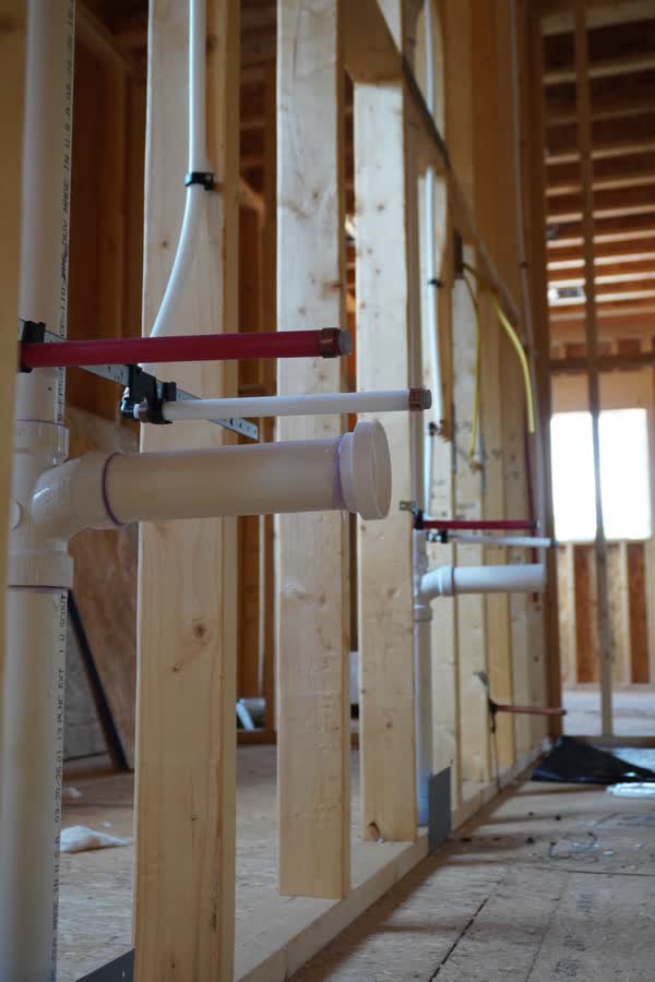 A full wall of PEX supply and PVC drain rough-in running the length of a framed corridor