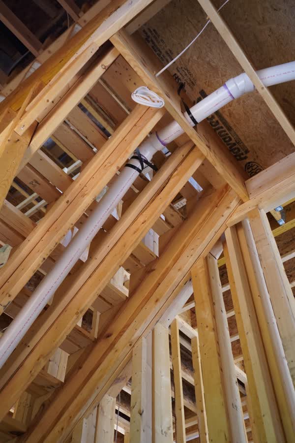Drain and vent piping carried up through the roof framing of a house under construction